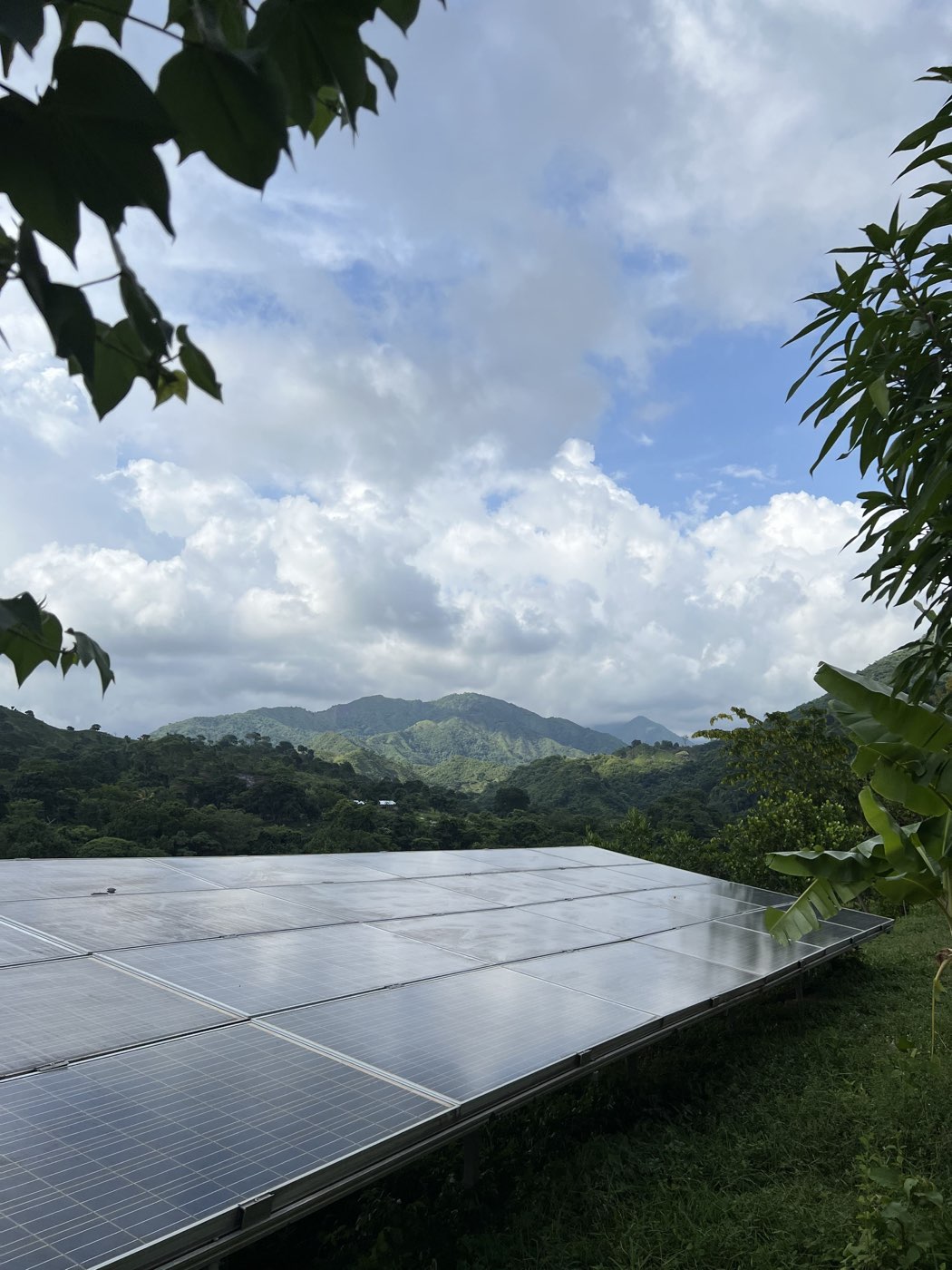 A GivePower solar array on a green hillside below forested mountains