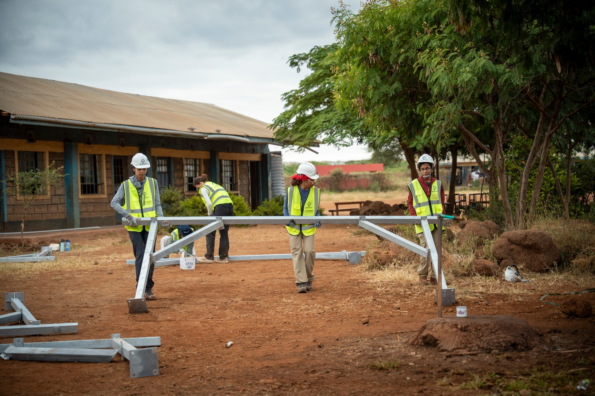 Volunteers in GivePower safety vests assembling a solar array frame at a rural school