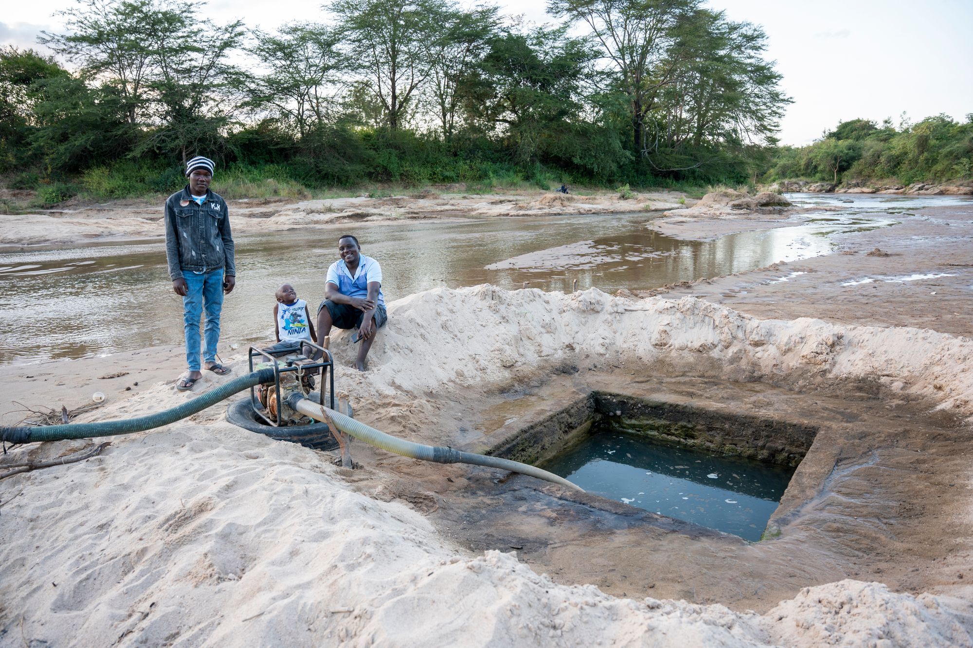 Community members beside a pump drawing water from a riverbed well